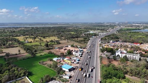 Aerial view of a busy Indian highway. It cuts through farmlands and developing areas, with a large l
