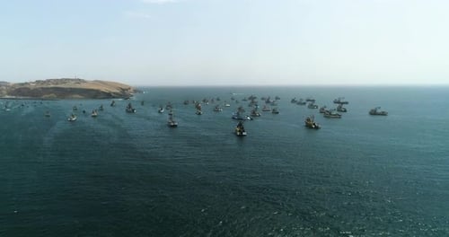 Aerial view approaching fishing ships anchored on the shore of sunny Huacho, Peru