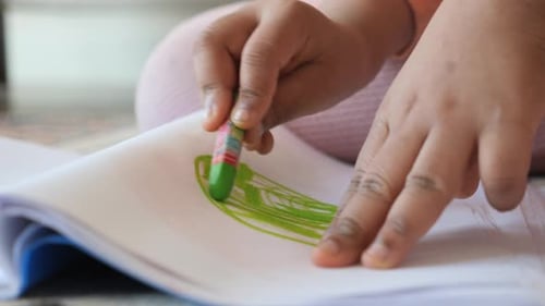 Close Up of a Child Hand Drawing with Colored Pencil on a Page