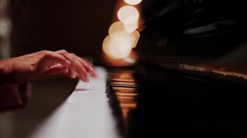 Close up of a woman's hands playing the piano with blurry lights on the background