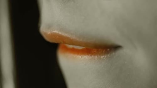 Orangefarbener Lippenstift auf den Lippen von jungen Mädchen/Teenager-Mädchen/Frauenmund beißt auf Lippe/Seite