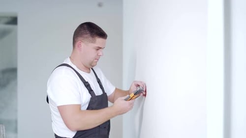 Male worker professional qualified electrician installs electrical outlet in apartment after repair.