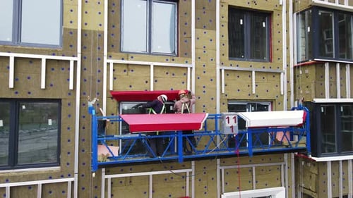 Approach at Worker in a Cradle Install the Window Trim of a Multi-storey Building under Construction