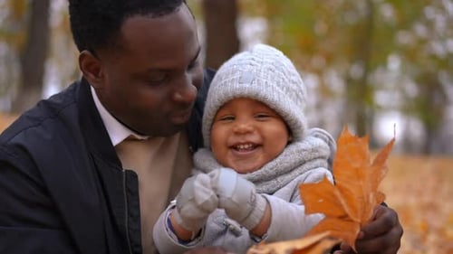 Lächelnder Vater küsst die Wange eines verspielten kleinen Sohnes, der am Herbsttag im Freien mit Kind sitzt