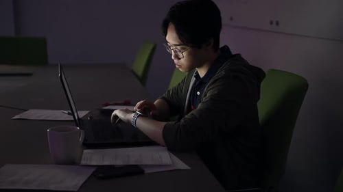 Young Man Working Late on Laptop in Dark Office