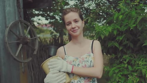 Lady in the garden. Young adult woman stands in the summer garden with flower pot and looks at the c