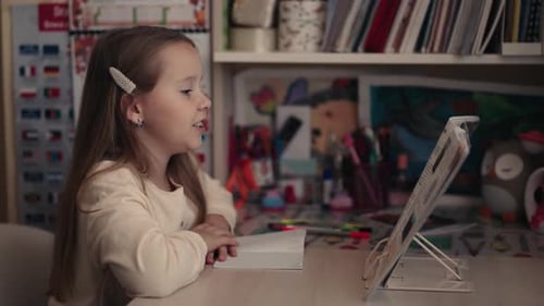 Young Girl Enjoys Reading a Book on a Stand at Her Desk in Her Bedroom