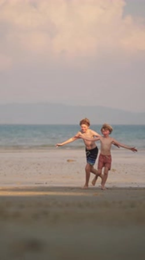 Two Boys Playfully Run Across The Shoreline