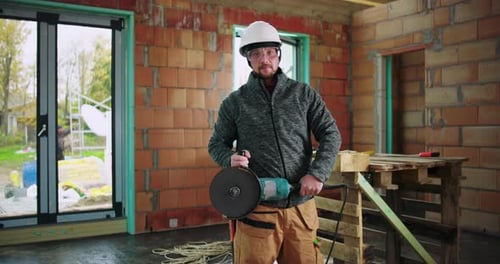 Construction worker holding angle grinder, ready for metal cutting task, safety helmet and