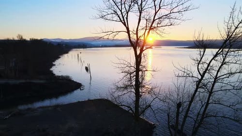 Drone slowly panning to the right behind trees with a beautiful sunset overlooking a gorgeous large