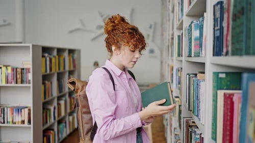 Une fille aux cheveux bouclés vient dans une étagère de la bibliothèque pour prendre un manuel