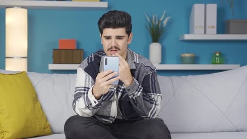Man on Couch Looking at Phone Sadly