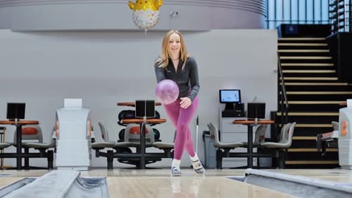 Smiling Woman in Sport Jacket Throws Violet Ball in Bowling Lane Slow Motion Shot