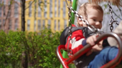 Slow Motion Closeup An Unrecognizable Woman Swings a Joyfully Laughing Little Boy on a Swing Joy on