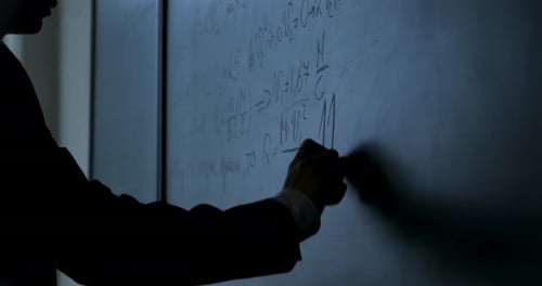 Silhouette Writes Math Equations on Chalkboard
