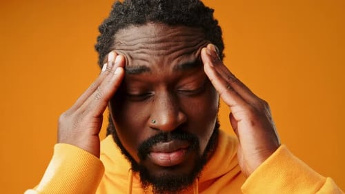 Man Rubbing Temples on Orange Background
