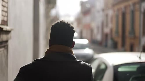 Back of elegant black man walking in city sidewalk during winter season removing scarf