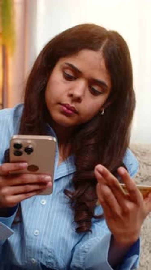 Indische Frau lächelt beim Online-Shopping mit Smartphone und Kreditkarte auf dem heimischen Sofa im Haus