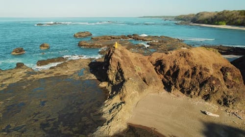 Woman walking on rocky outcrop by turquoise Pacific Ocean in Costa Rica