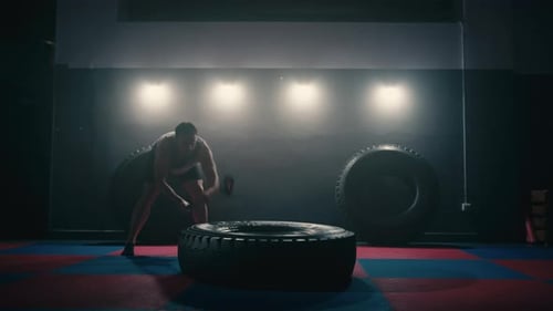 Muscular Man Hits Tire with Sledgehammer in Gym