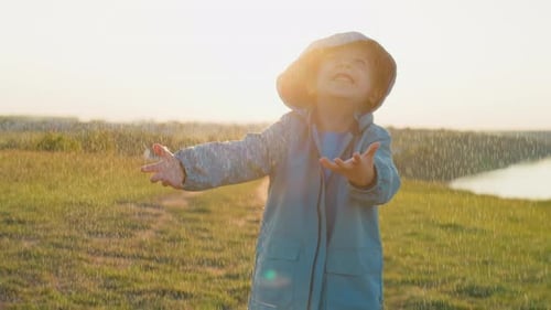 Kid Holds Palms Under Warm Spring Rain in Field