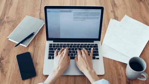 Person, die auf einem Laptop mit Dokumenten und einer Kaffeetasse auf einem Holztisch tippt