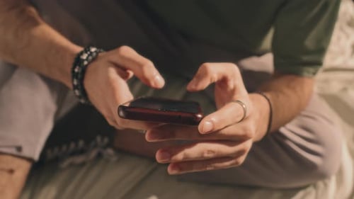 Close Up Of Sunlit Male Hands Typing On Smartphone, Bedroom