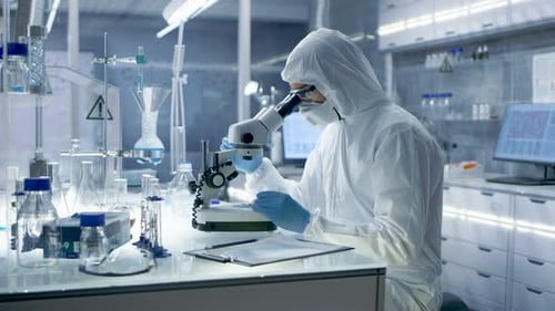 Scientist in Protective Suit Examining Slide Under Microscope