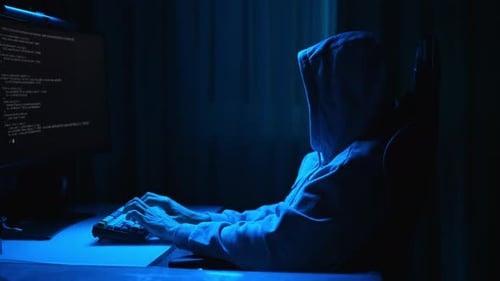 Hooded Figure Typing at Computer in Dark Room