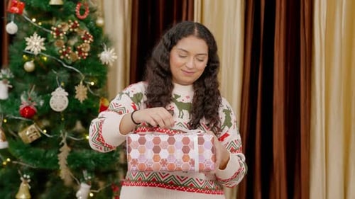 Woman Unwraps Gift Next to Christmas Tree