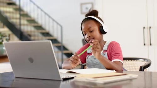 In school, child wearing headphones studying with laptop and writing in notebook