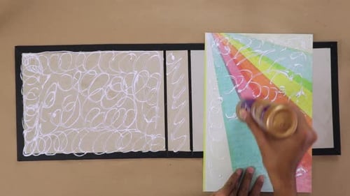 Hand gluing rainbow-colored paper to a scrapbook cover for a DIY project, close-up view