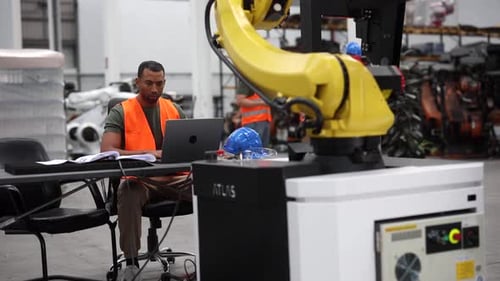 Ingénieur en robotique programmant un bras robotique à l'aide d'un ordinateur portable dans une usine à la pointe de la technologie, sh