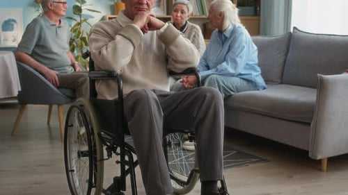 Portrait of Elderly Man in Wheelchair with Friends in Nursing Home Lounge