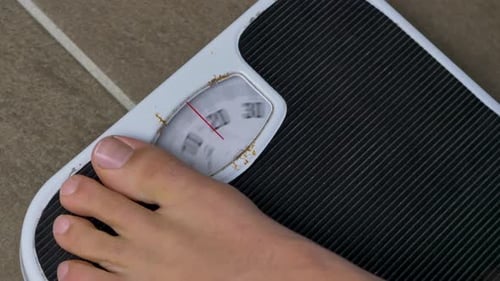 Close-up slow motion shot of feet stepping onto bathroom scales weight measurements body human foot
