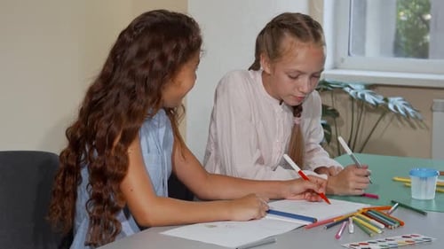 Zwei Schulfreunde unterhalten sich freudig, während sie im Kunstunterricht farbenfrohe Zeichnungen erstellen