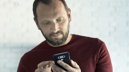 Bearded man using smartphone indoor with neutral look