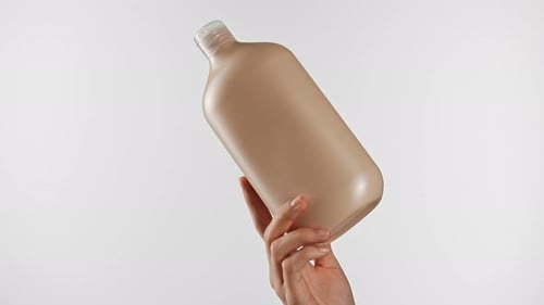 Hand Holding Beige Shampoo Bottle Against White Background