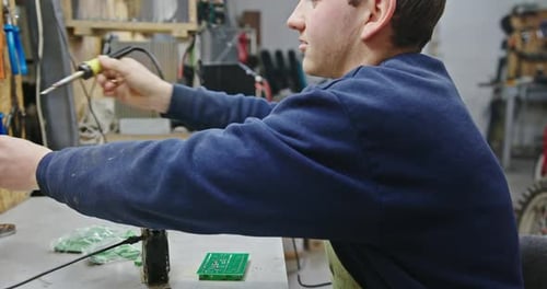 Mann lötet Mikrochip in der Werkstatt Seitenansicht Männlicher Techniker sitzt am Tisch und lötet