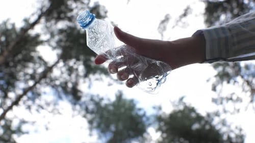 Hand Discards Plastic Bottle in Forest