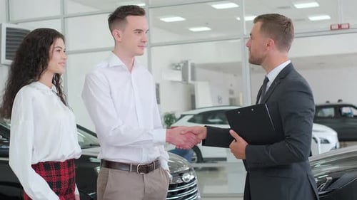 A Man in a Dress Shirt is Discussing Vehicles with a Woman and a Man in a Showroom Buying a New Car