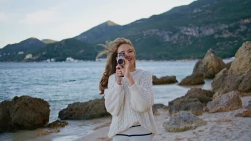 Woman Films with Vintage Camera on Rocky Beach