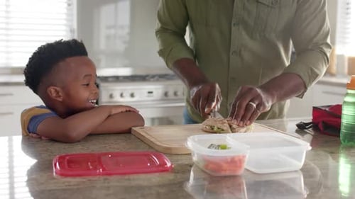 African american grandfather making packed lunch with grandson in kitchen for school, slow motion
