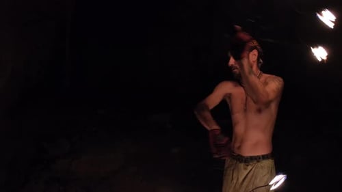 A young male performer dances with a fire fan. Exciting fire show in a dark cave.