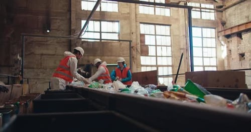 Side View of Waste Recycling Plant Workers in Special Uniforms Laying Out and Sorting Plastic