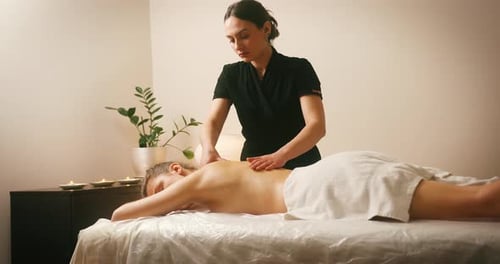 Glückliche junge Frau liegt im Spa-Salon auf dem Bett und genießt Rückenmassage Kosmetikerin massiert Frau