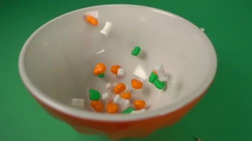 Colorful Halloween Candy Falling into Bowl on Green