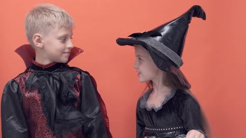 Halloween Boy and Girl Hiss at Each Other on Orange Background Trick or Treat Kid in Vampire Witch