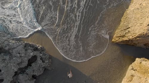 Drone aerial view of young woman walking on the beach towards the sea from top down in Nerja