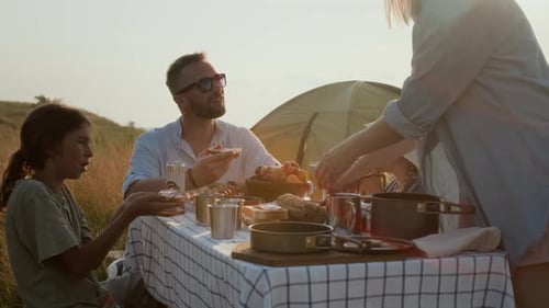 Mother Serving Food for Family at Campsite Dinner on Sunny Lakeshore